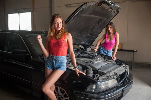 Дві дівчини стоять біля машини в авторемонтному магазині — стокове фото