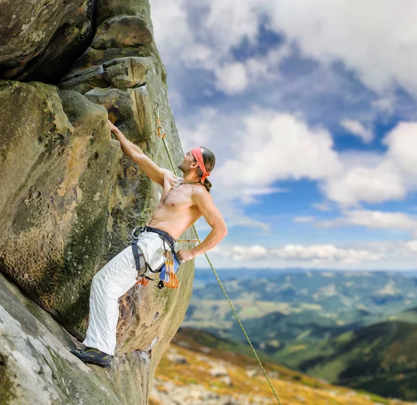 Masculino escalador de rocha escalada com corda em uma parede rochosa — Fotografia de Stock