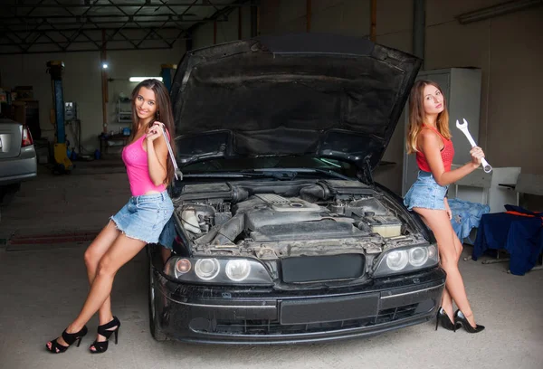 Две девушки стоят у машины в автомастерской — стоковое фото