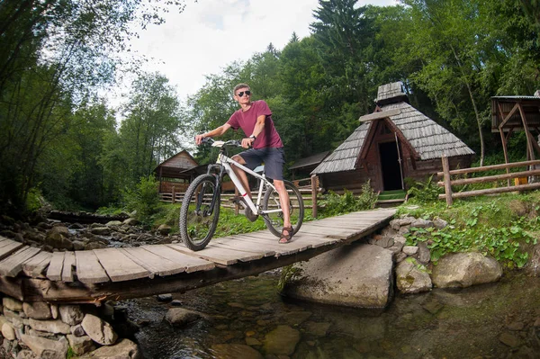 L'uomo va in bicicletta attraverso un ponte di legno su un fiume — Foto Stock