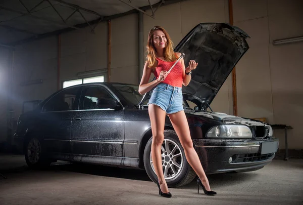 Сексуальная леди, стоящая возле машины в автомастерской — стоковое фото