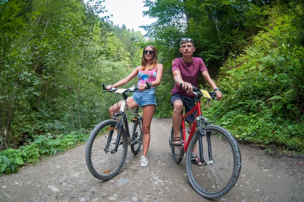 Happy couple ride on a mountain asphalt road on bikes — Stock Photo, Image