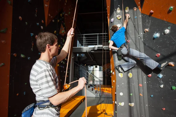 Belayer segurando o alpinista na parede de rocha dentro de casa — Fotografia de Stock