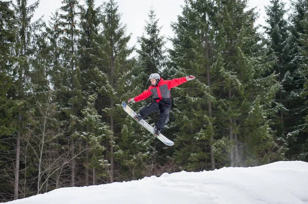 Pensionista masculino no snowboard pulando sobre a encosta — Fotografia de Stock