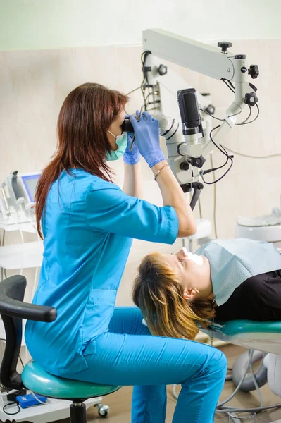 Dentiste féminine travaillant au microscope dans une clinique dentaire moderne — Photo