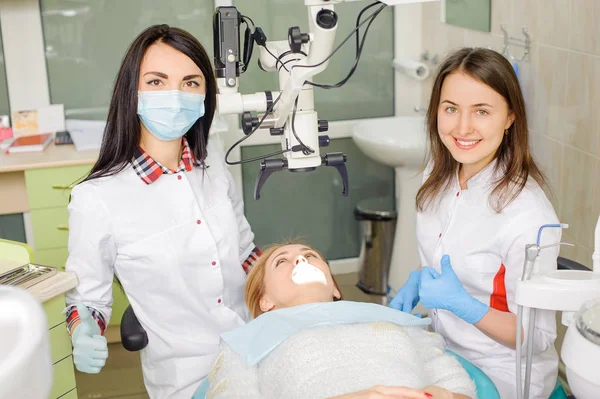 女牙医治疗龋在牙医办公室使用显微镜 — 图库照片