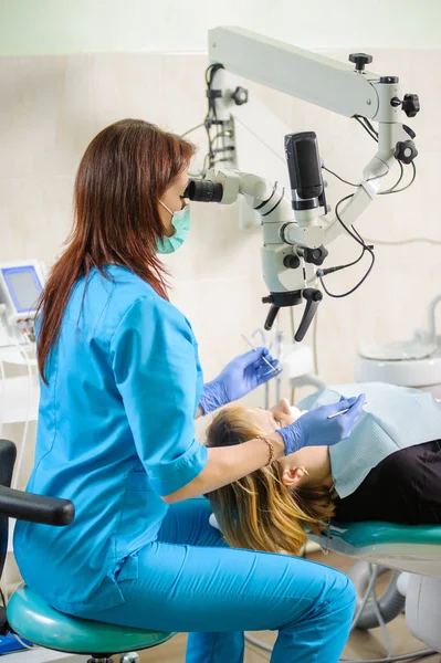 Dentiste féminine travaillant au microscope dans une clinique dentaire moderne — Photo