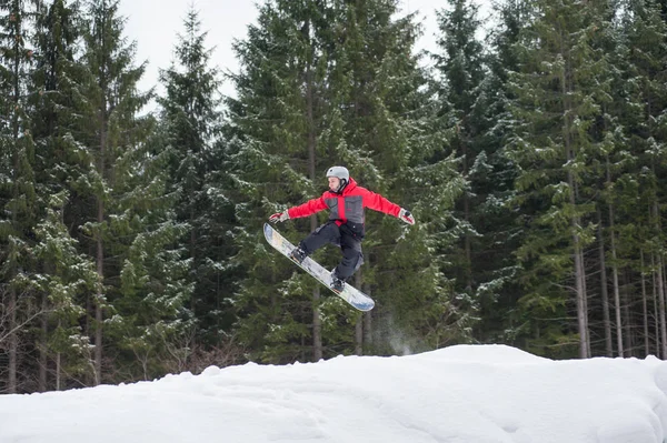 Pensionista masculino no snowboard pulando sobre a encosta — Fotografia de Stock