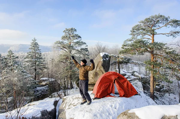 Male climber nearly his tent on the top of rock