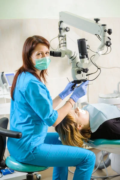 Dentiste féminine travaillant au microscope dans une clinique dentaire moderne — Photo