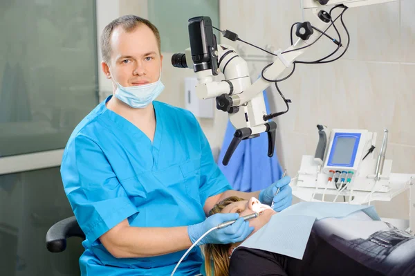 在现代的牙医诊所与显微镜工作的男性牙医 — 图库照片