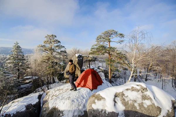 Male climber nearly his tent on the top of rock