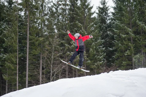 Pensionista masculino no snowboard pulando sobre a encosta — Fotografia de Stock