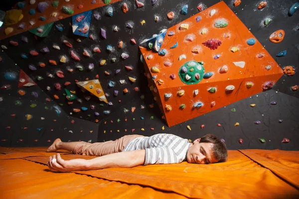 Escalador macho cansado en la alfombra cerca de la pared de roca en el interior —  Fotos de Stock