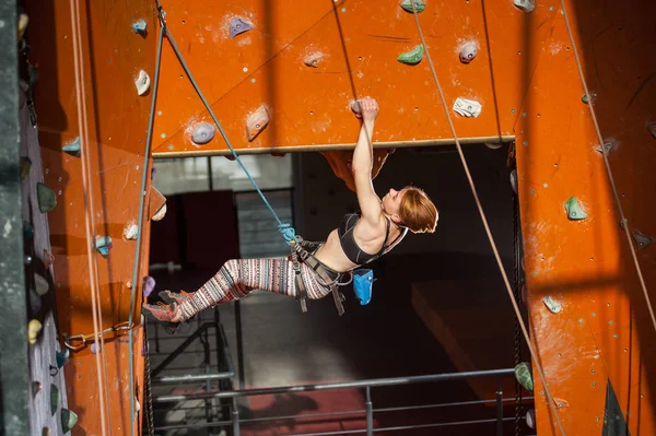 Female climber is climbing up on indoor rock-climbing wall