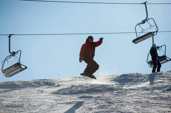 Homem snowboarder pulando na estância de esqui contra ski-lift — Fotografia de Stock