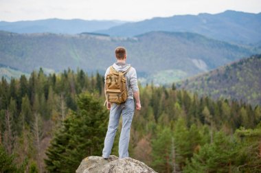 Kaya tepe üzerinde kahverengi sırt çantası ile erkek dağcı
