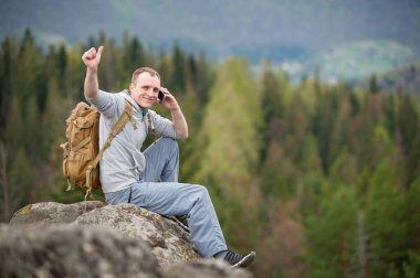 Kaya tepe üzerinde kahverengi sırt çantası ile erkek dağcı