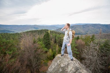 Kaya tepe üzerinde kahverengi sırt çantası ile erkek dağcı