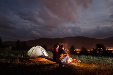 Bulutlu gökyüzü altında şenlik ateşi başına oturmuş Romantik Çift