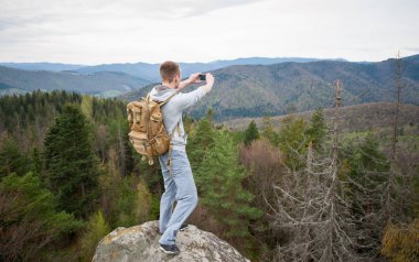 Kaya tepe üzerinde kahverengi sırt çantası ile erkek dağcı