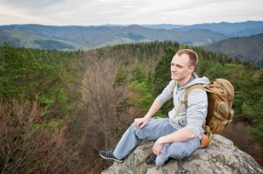 Kaya tepe üzerinde kahverengi sırt çantası ile erkek dağcı