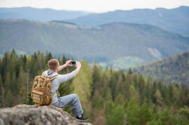 Kaya tepe üzerinde kahverengi sırt çantası ile erkek dağcı