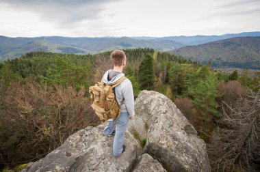 Kaya tepe üzerinde kahverengi sırt çantası ile erkek dağcı