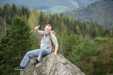 Kaya tepe üzerinde kahverengi sırt çantası ile erkek dağcı