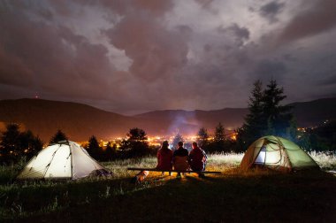 Üç turist panoları yakınında çadır kamp ateşi etrafında oturan