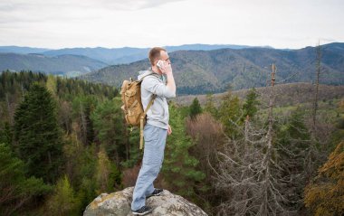 Kaya tepe üzerinde kahverengi sırt çantası ile erkek dağcı