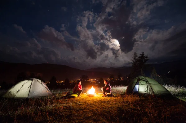 Homme et femme assis près de deux tentes dans la nuit — Photo