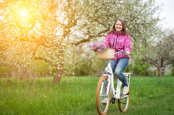 Mujer ciclista montando una bicicleta blanca vintage en el jardín de primavera — Foto de Stock