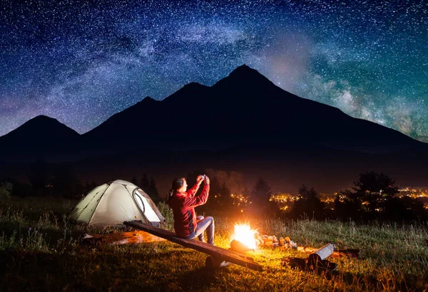 Feminino sentado perto da tenda e faz foto do céu estrelado — Fotografia de Stock