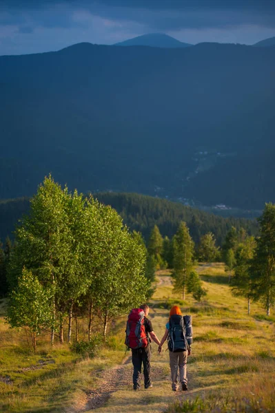 Vue arrière couple touristes avec sacs à dos marchant le long d'une belle région de montagne se tenant la main. Lifestyle vacances actives concept montagnes paysage sur fond — Photo