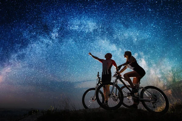 Couple cyclists with mountain bikes at night under starry sky — Stock Photo, Image