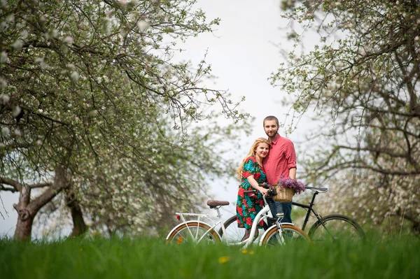 Любящие молодые пары с велосипедами в весеннем саду — стоковое фото