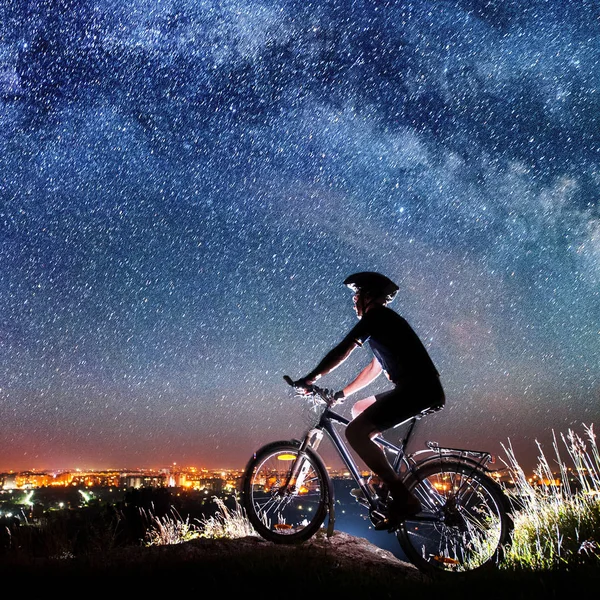 Cyclist riding bike in the night under starry sky