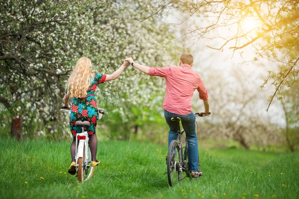 Любящие молодые пары катаются на велосипедах в весеннем саду — стоковое фото