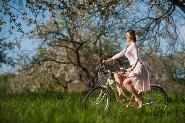 Hermosa ciclista femenina con bicicleta retro en el jardín de primavera — Foto de Stock