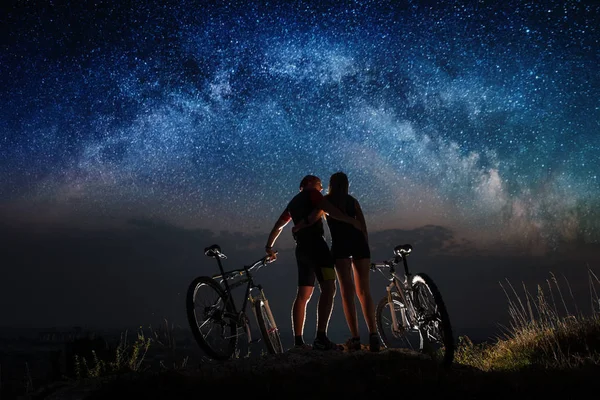 Couple cyclists with mountain bikes at night under starry sky — Stock Photo, Image