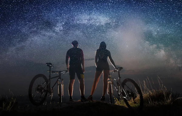 Couple cyclists with mountain bikes at night under starry sky — Stock Photo, Image