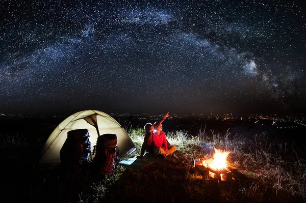 Noche de camping cerca de la ciudad. Pareja joven sentada cerca de la fogata — Foto de Stock