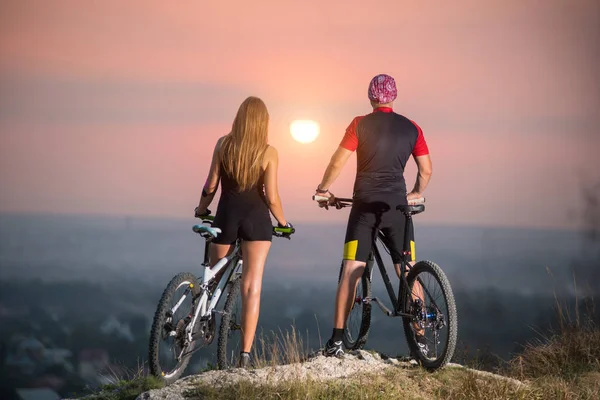 Pár kerékpárosok és mountain bike-dombon napnyugtakor — Stock Fotó