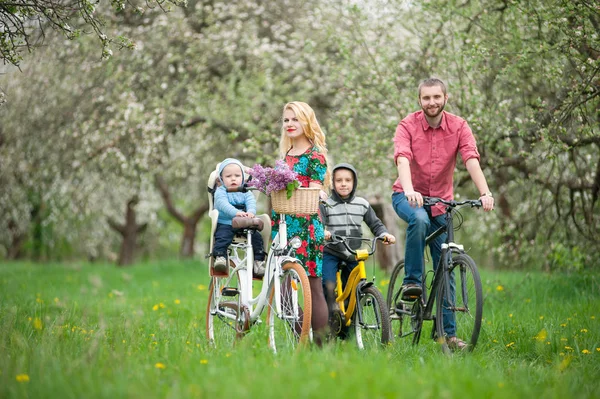 Familia feliz en una bicicleta en el jardín de primavera — Foto de Stock