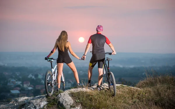 Couple bicyclist with mountain bikes on the hill at sunset — Stock Photo, Image