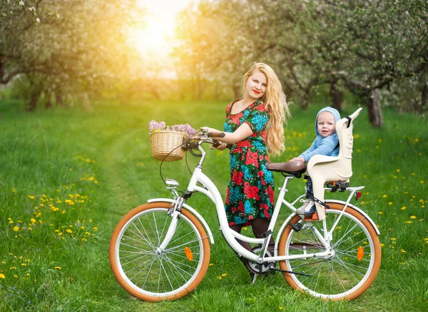 Blond kobieta z miasta rowerem z dzieckiem w fotelu rowerów — Zdjęcie stockowe