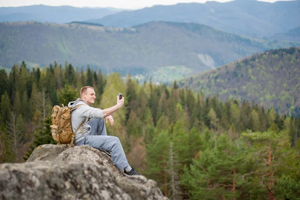 Alpinista masculino com mochila marrom no pico da rocha — Fotografia de Stock