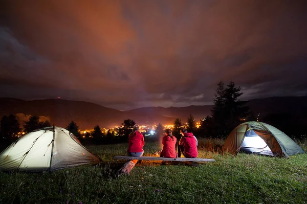 Friends sitting on bench and watching fire together beside camping