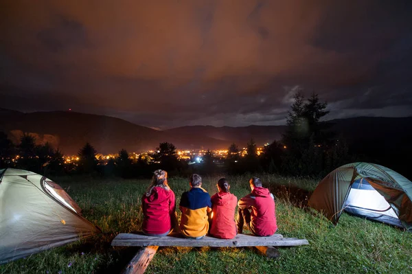 Turister titta på brand grupp bredvid läger och tält i mörkret — Stockfoto